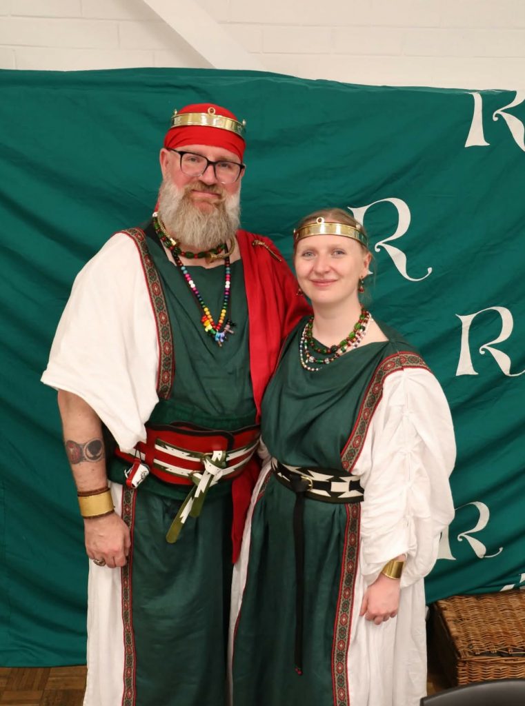 a photo of Proconsul Roman (Left) and Proconsul Tullia (right). They are dressed in green and white roman style tunica, stacked necklaces, and coronets.